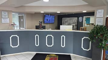 A hotel reception area with a check-in counter, a television mounted on the wall, and a digital screen displaying information.