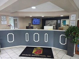 Zona de recepción de un hotel con mostrador de check-in, un televisor montado en la pared y una pantalla digital mostrando información.