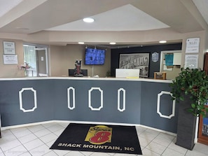 Zona de recepción de un hotel con mostrador de check-in, un televisor montado en la pared y una pantalla digital mostrando información.