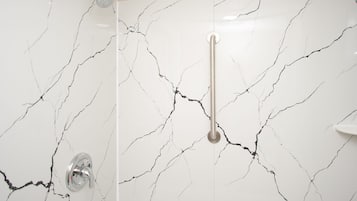 Een badkamer met een witte marmeren wand met zwarte aderen, een handdouche en een verticale greepstaaf.