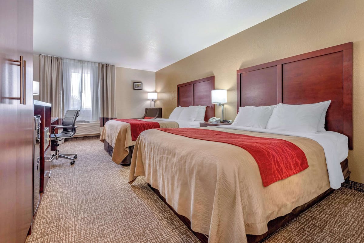 Quarto de hotel com duas camas, uma escrivaninha, uma cadeira e janela com cortinas.