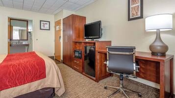 A hotel room with a bed, a desk with a computer, a television, a microwave, and a lamp.
