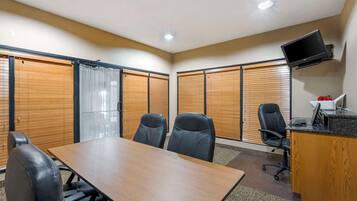 Uma sala de conferências com uma mesa comprida, quatro cadeiras, uma escrivaninha com computador e uma televisão fixada na parede.