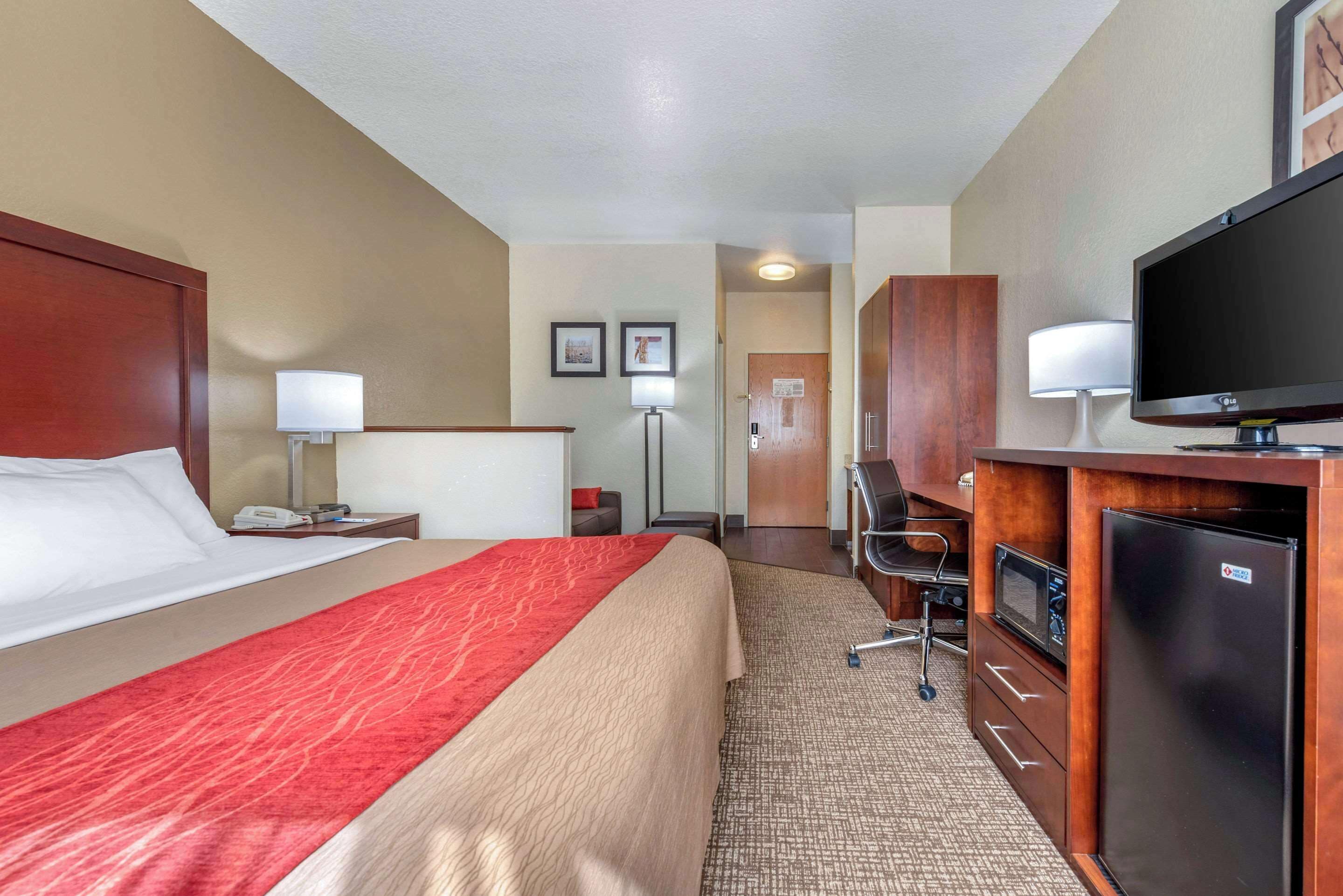 Habitación de hotel con una cama grande, un escritorio con computadora, refrigerador, microondas y televisión.
