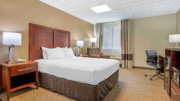 A hotel room with a large bed, bedside tables with lamps, a desk with a chair, and a window with curtains.