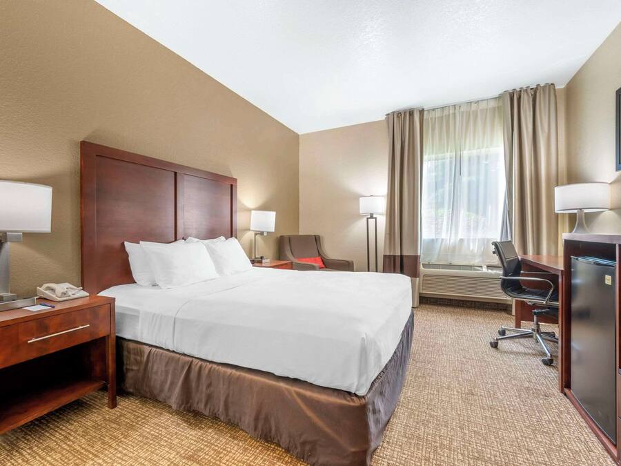 A hotel room with a large bed, bedside tables, a desk, a chair, and a TV.