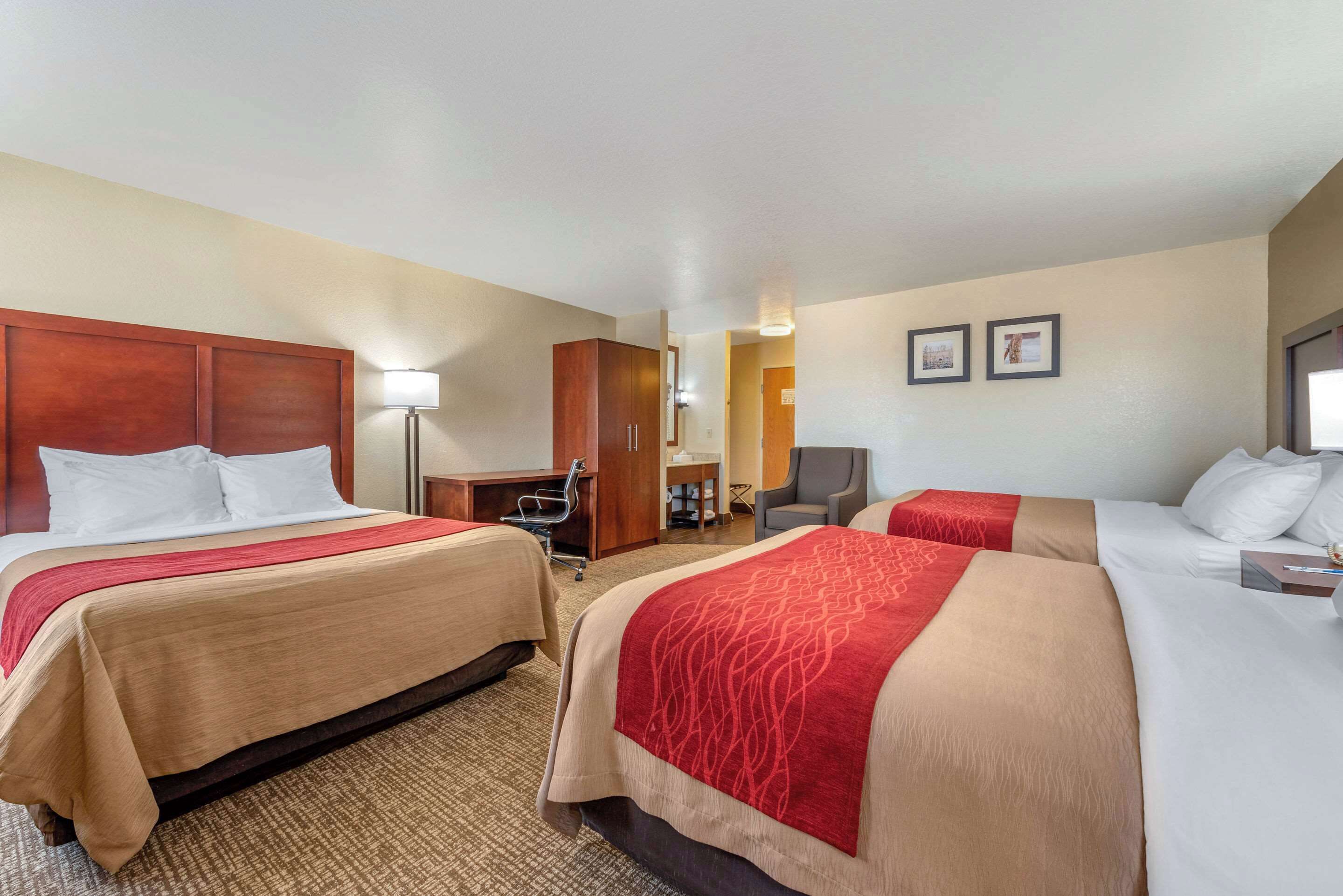 A hotel room with two beds, a desk, a chair, and a lamp.