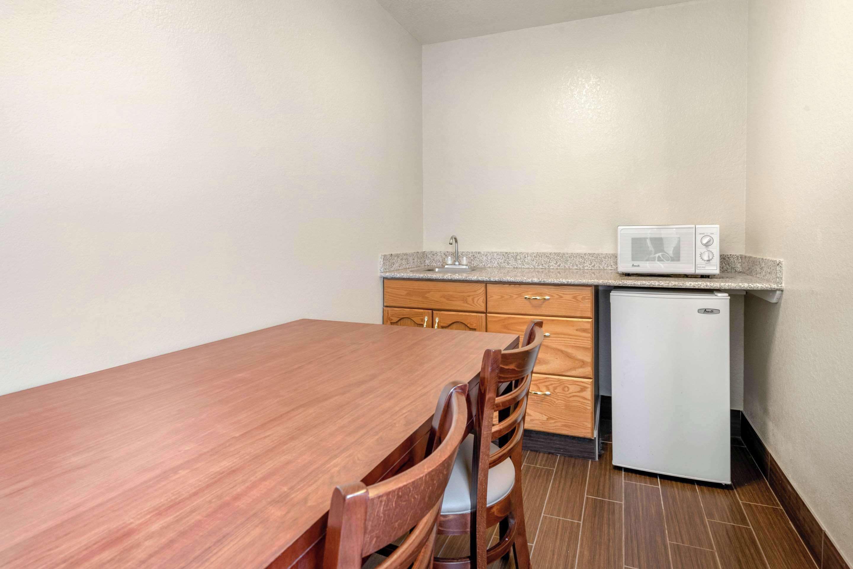 Una cocina compacta con una mesa de comedor de madera, sillas, microondas y refrigerador.