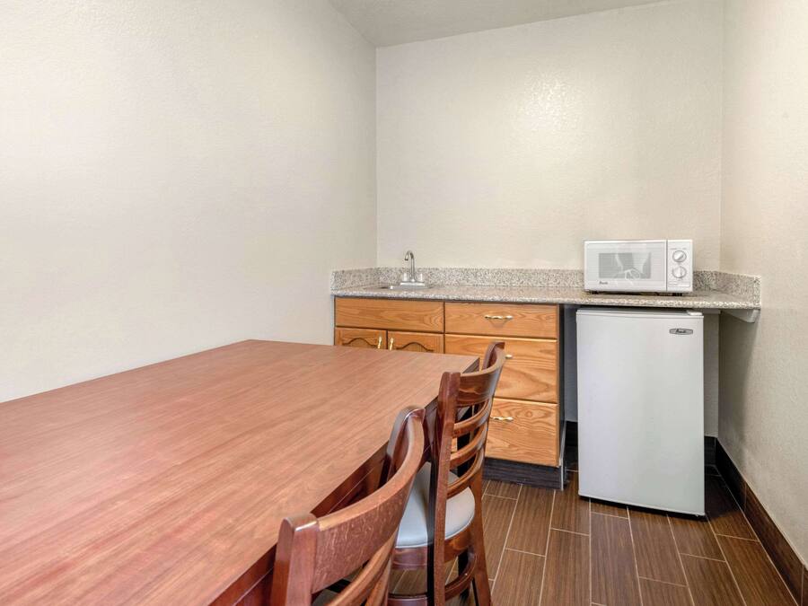 A compact kitchen with a wooden dining table, chairs, a microwave, and a refrigerator.