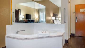 Un baño de hotel con un espejo grande, una bañera, un tocador con lavabo y una puerta con manija.
