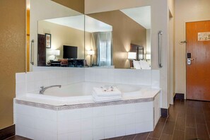 A hotel bathroom with a large mirror, a bathtub, a vanity with a sink, and a door with a handle.