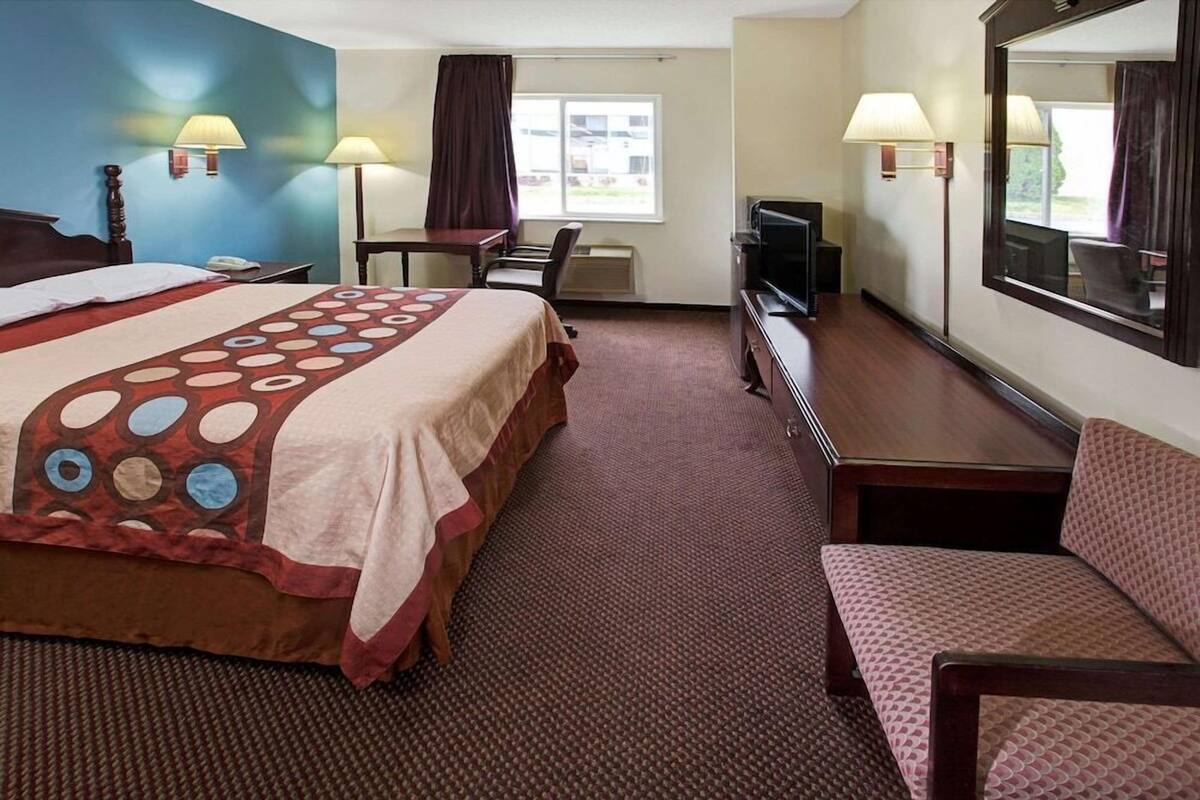 Una habitación de hotel con una cama, un escritorio, una silla, un televisor y un espejo grande.