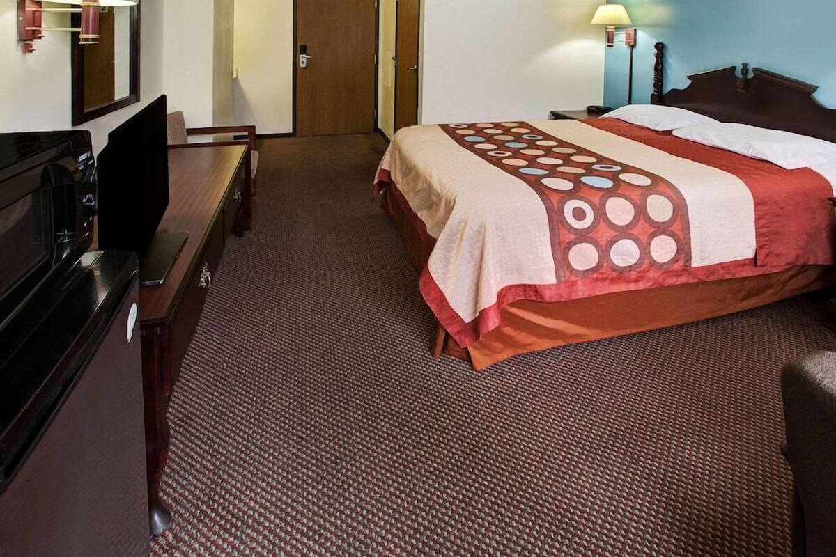 Habitación de hotel con cama, escritorio con televisor, puerta y lámpara.