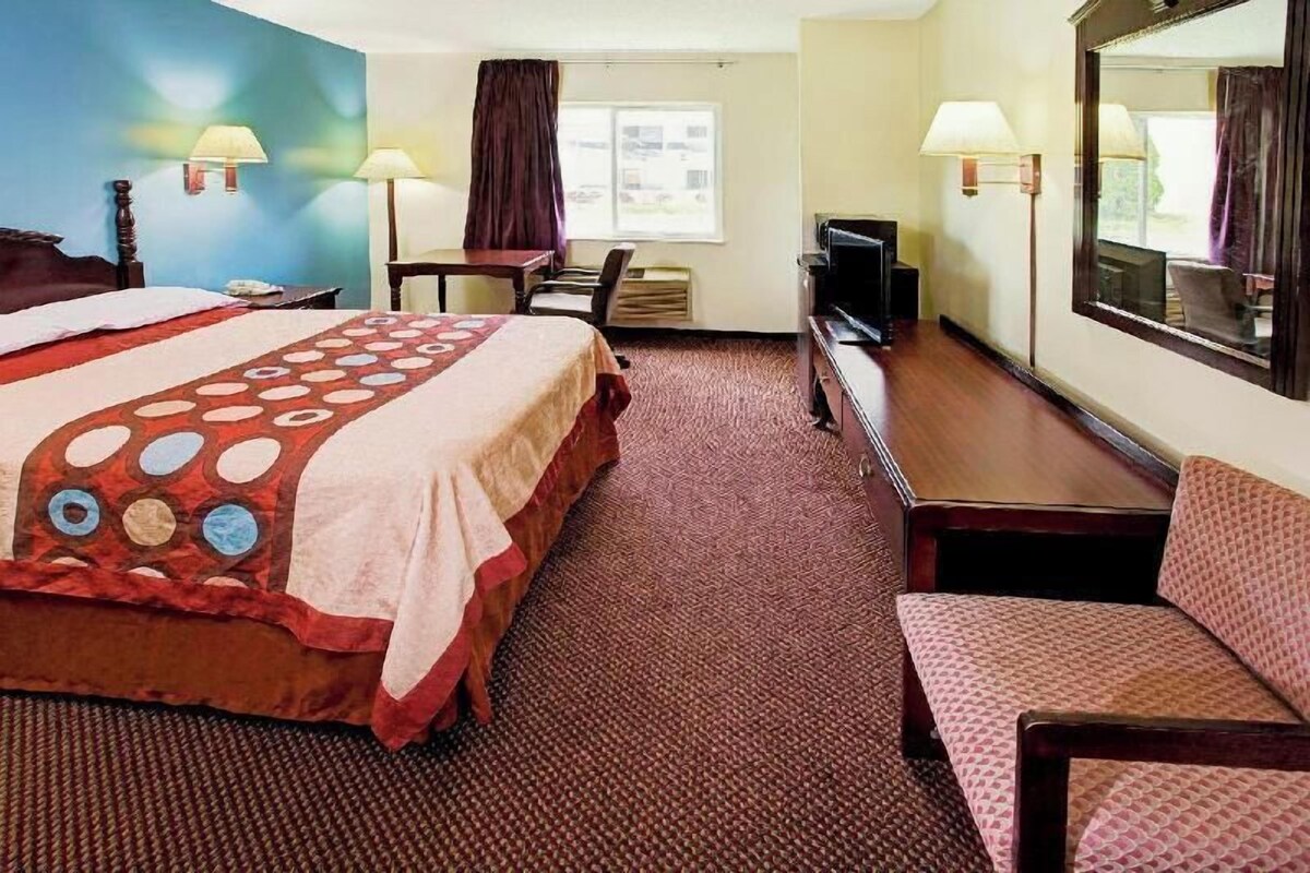 A hotel room with a large bed, a desk, a chair, a television, and a window.