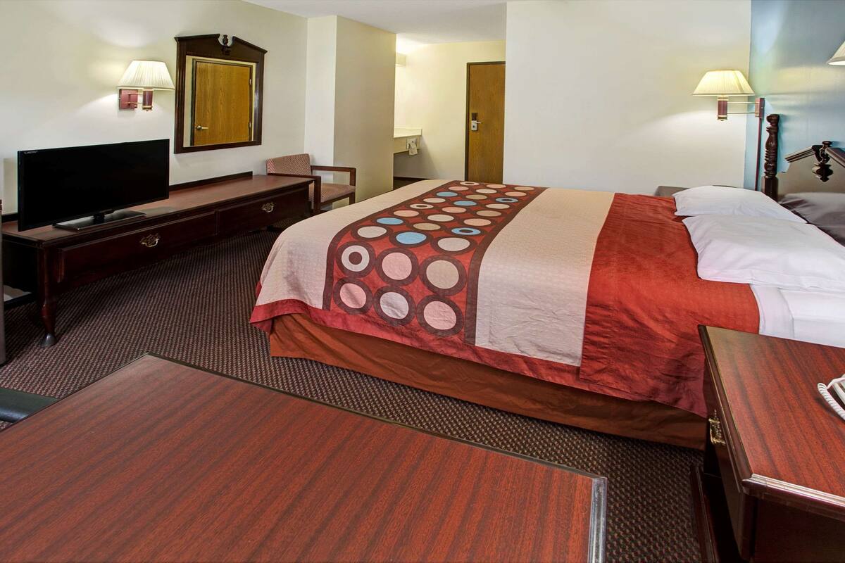 Una habitación de hotel con una cama, televisión, escritorio y silla.