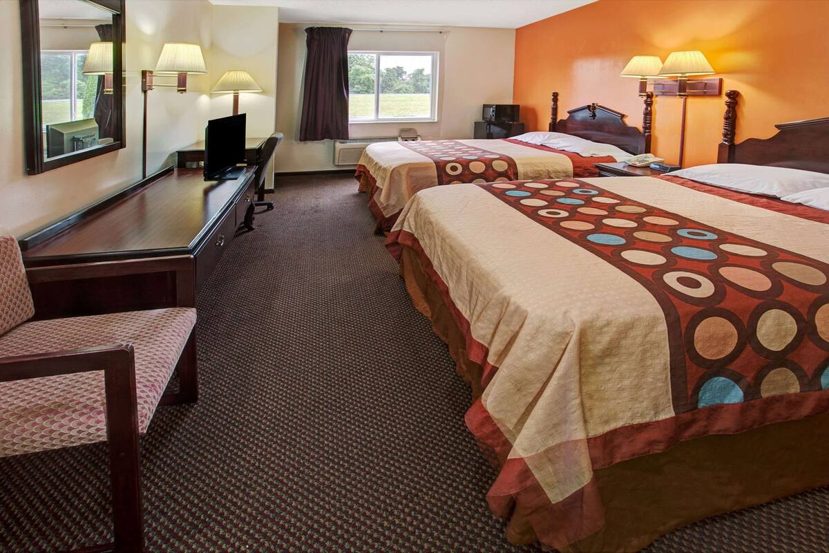 Una habitación de hotel con dos camas, un escritorio, una silla, un televisor y una ventana con cortinas.