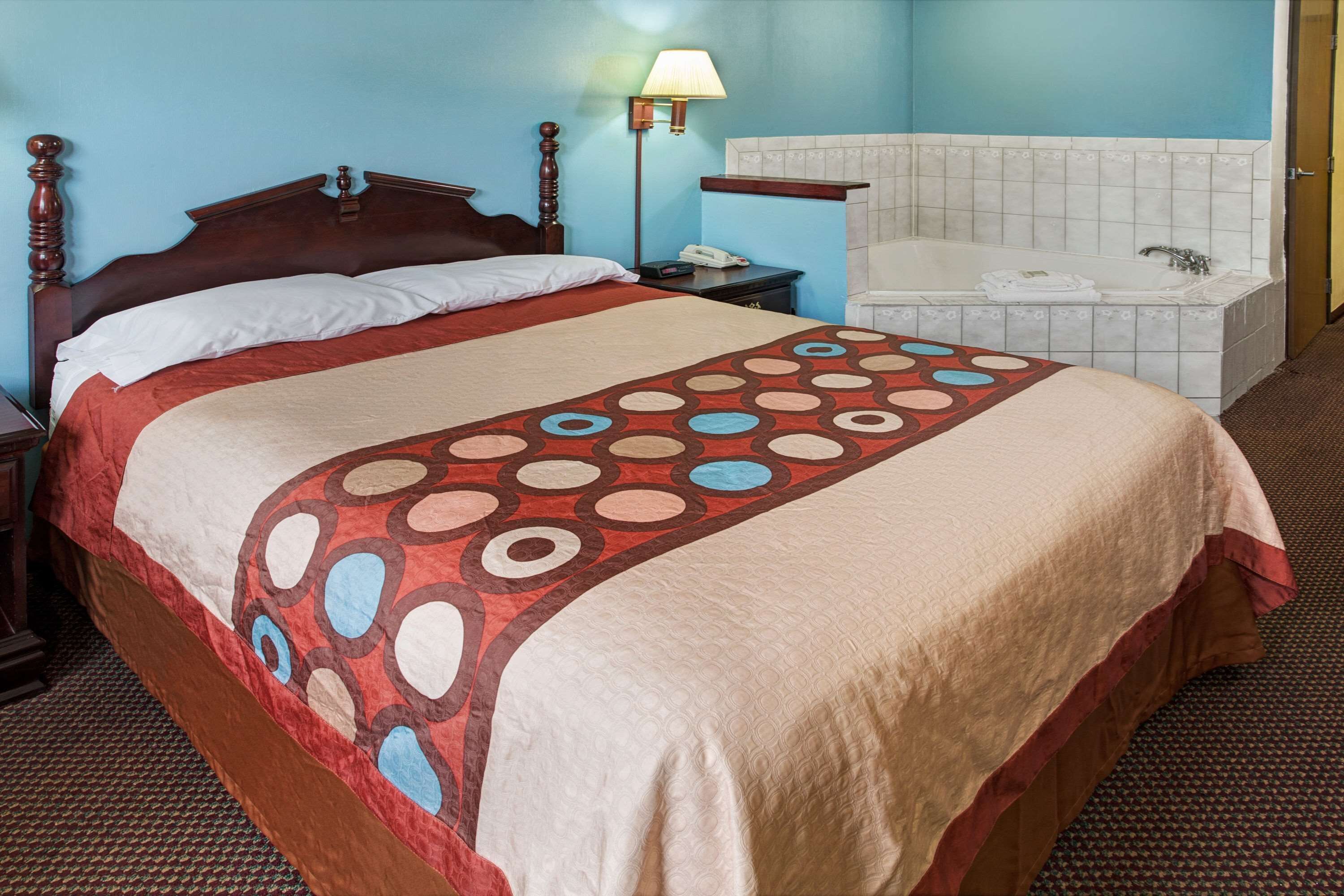 A hotel room with a large bed, a nightstand, a lamp, a bathroom with a bathtub, and a door.