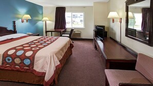 Ein Hotelzimmer mit einem großen Bett, einem Schreibtisch mit Stuhl, einem Fernseher und einem Spiegel.