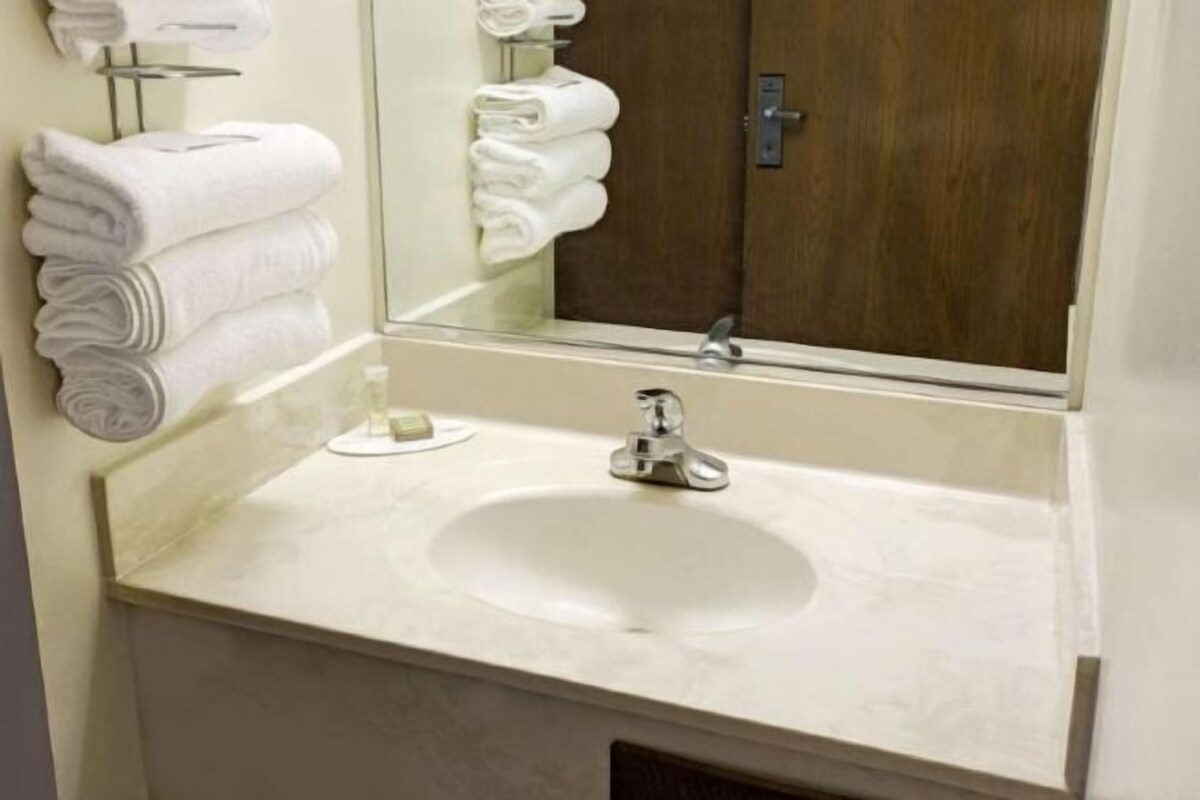 A bathroom with a sink, mirror, and stacked towels.