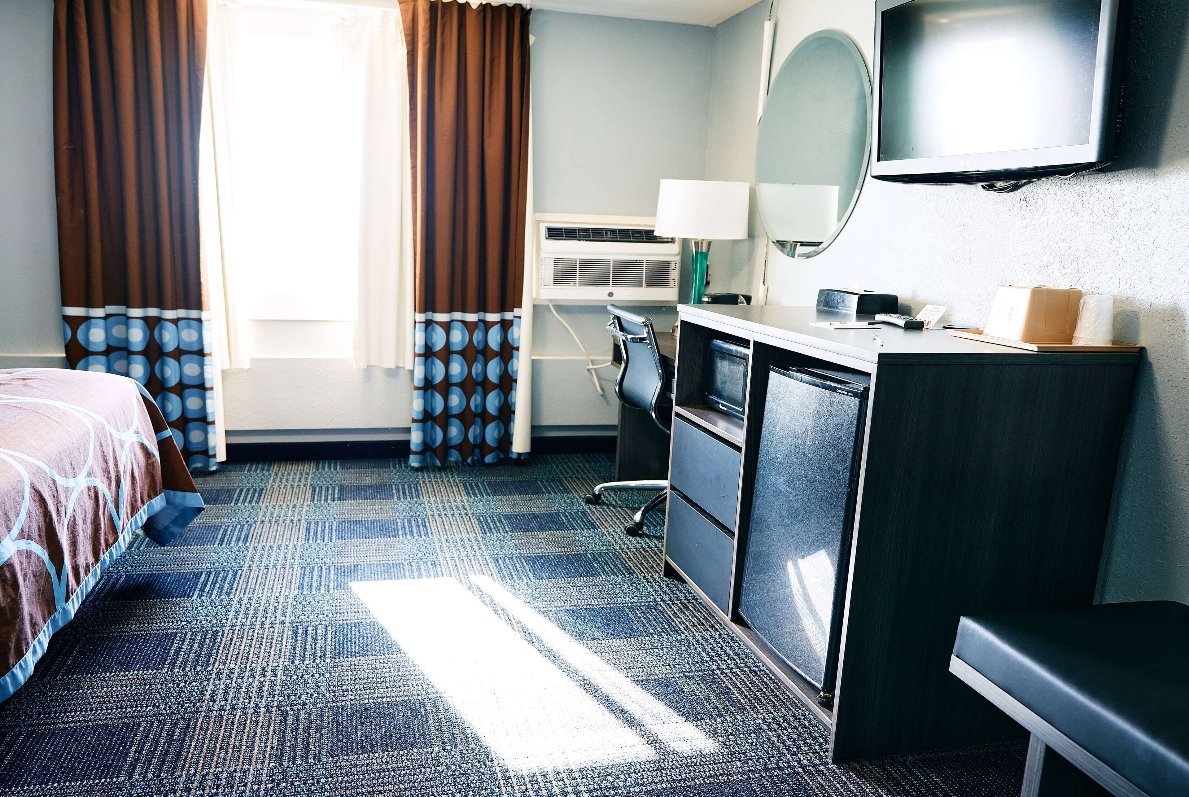 A hotel room with a bed, desk, chair, TV, and a window with curtains.