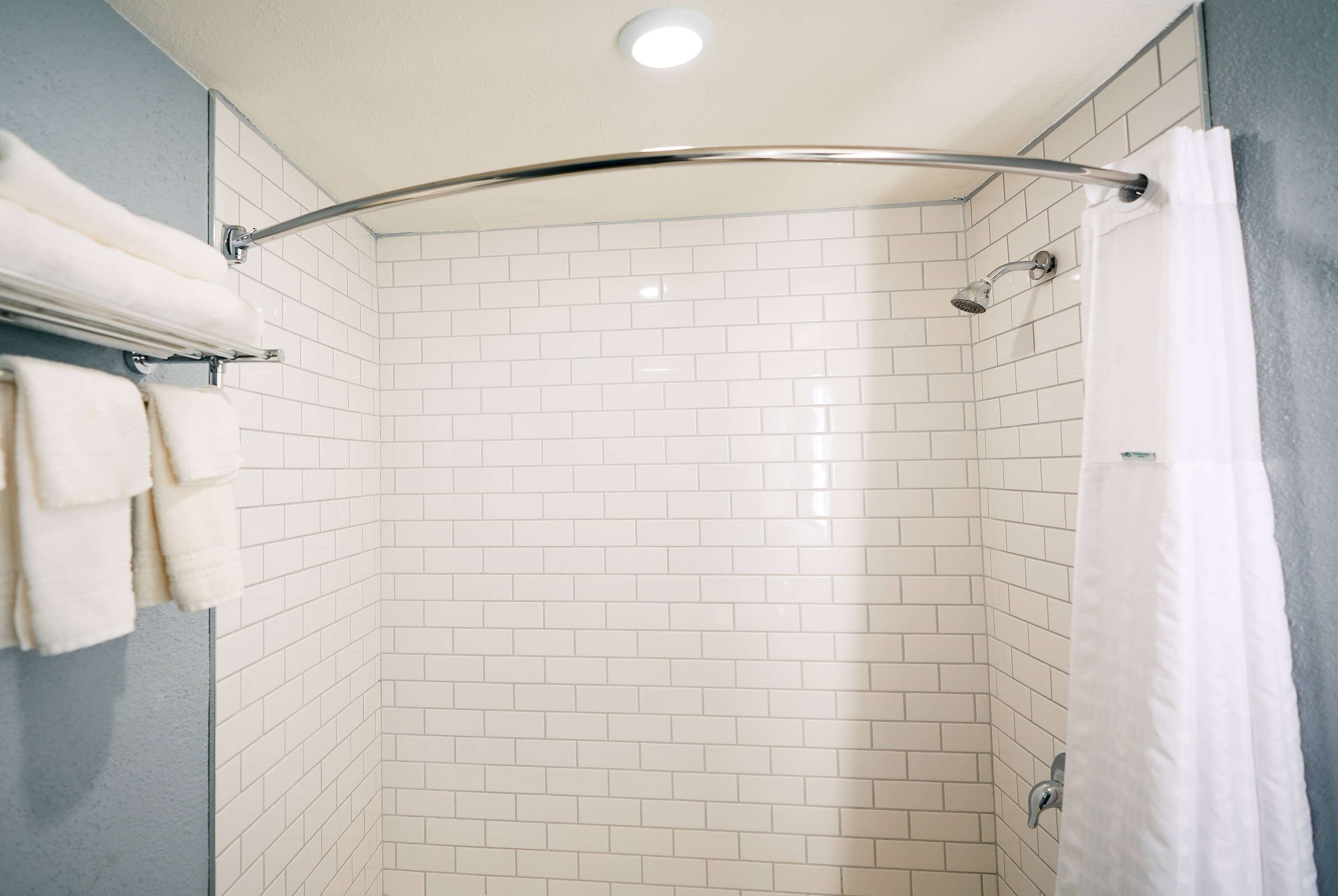 A shower with white tiled walls, a chrome showerhead, and a white towel rack with towels.