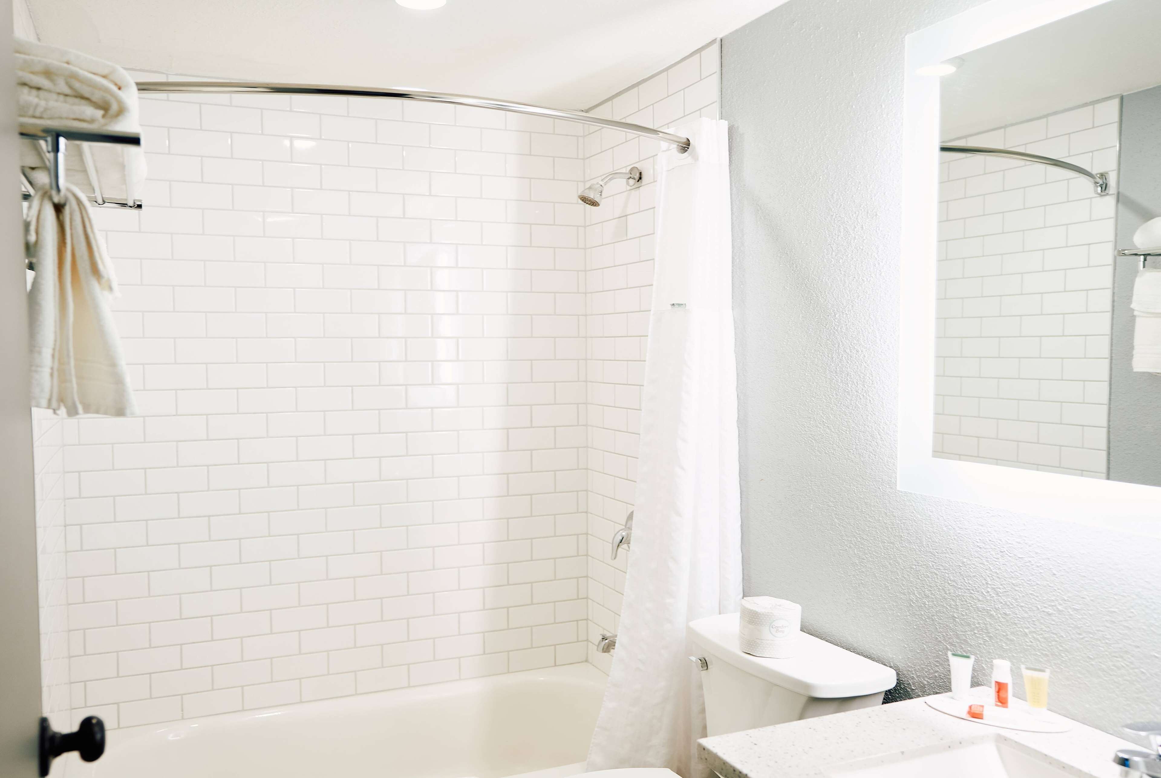 A modern bathroom with white subway tiles, a glass shower enclosure, a bathtub, and a toilet.