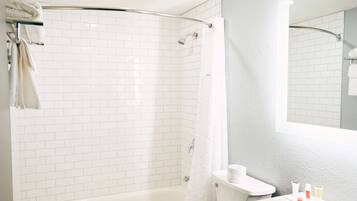 A modern bathroom with white subway tiles, a glass shower enclosure, a bathtub, and a toilet.