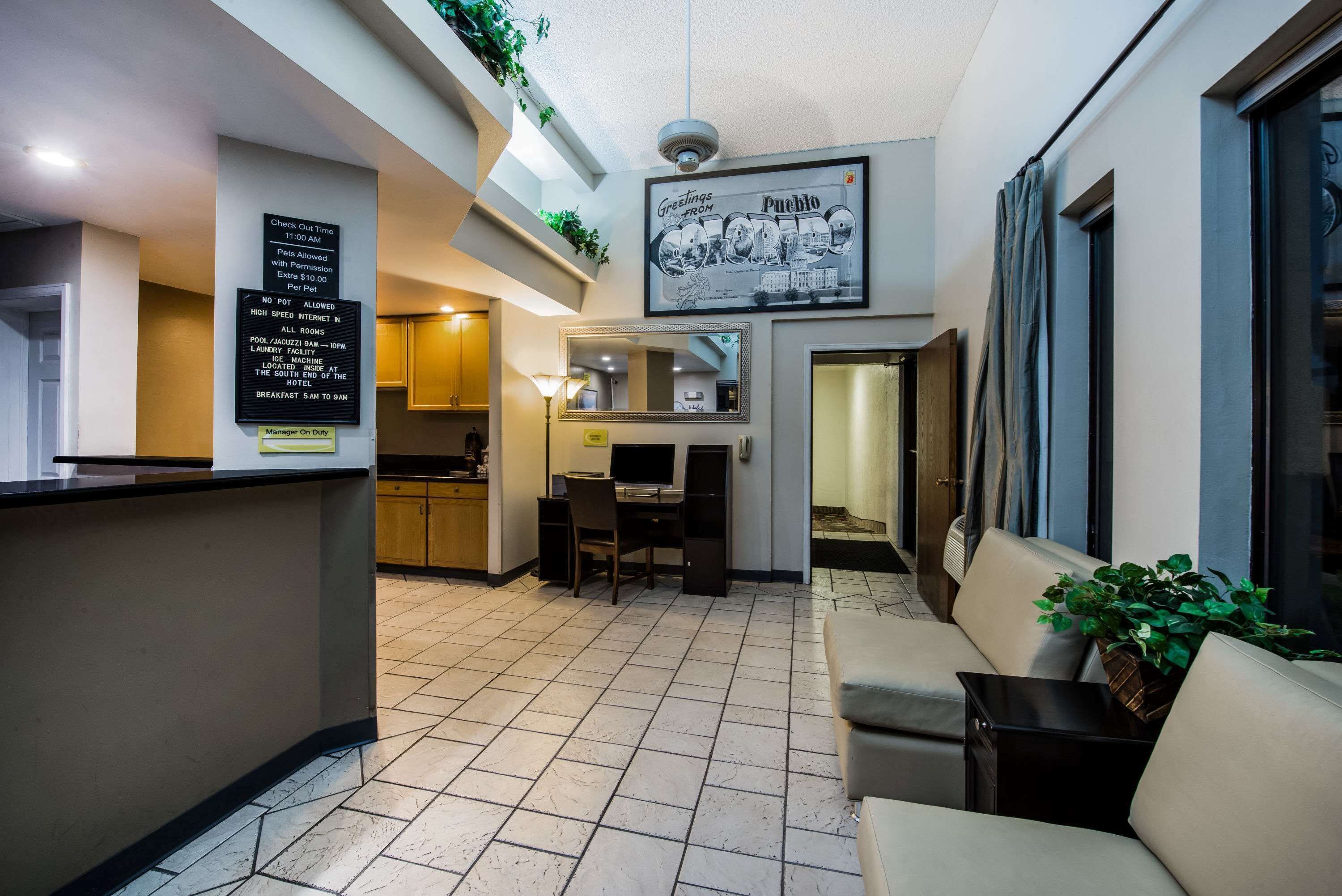 A hotel lobby with a reception desk, a dining area, and a seating area. There are signs indicating check-out time and pet policy.