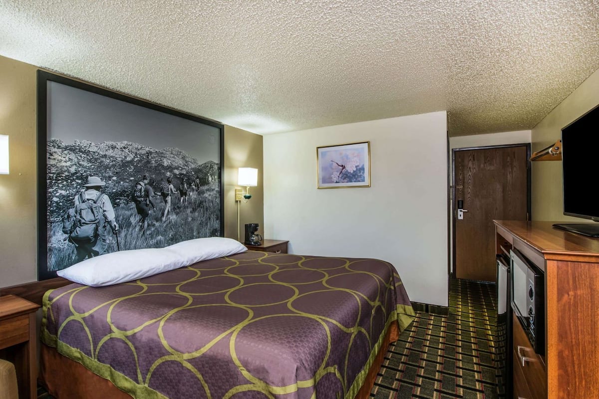 Una habitación de hotel con una cama grande, televisión, escritorio y una lámpara de pared.