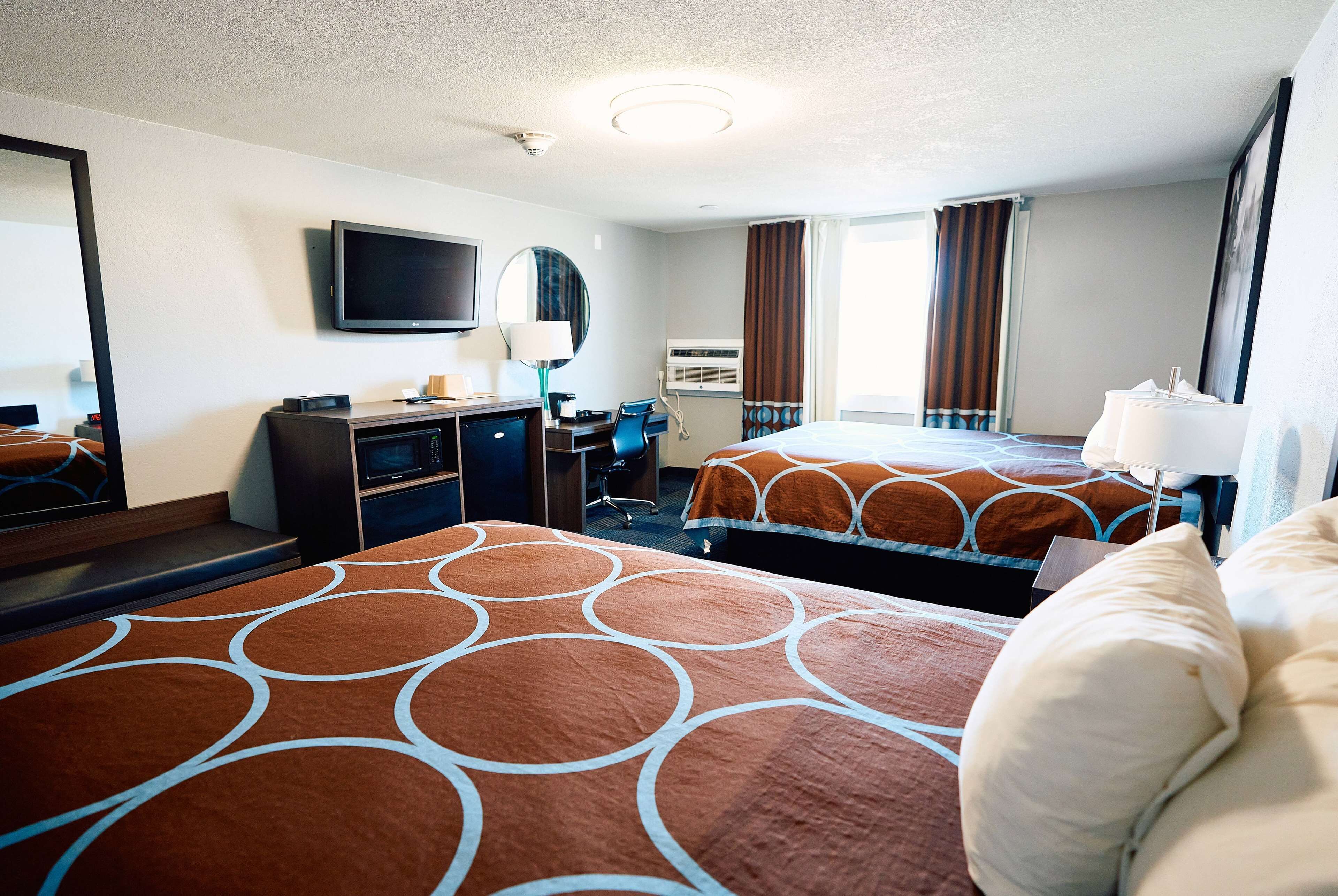 Habitación de hotel con dos camas, un escritorio, una silla, un televisor y un espejo.