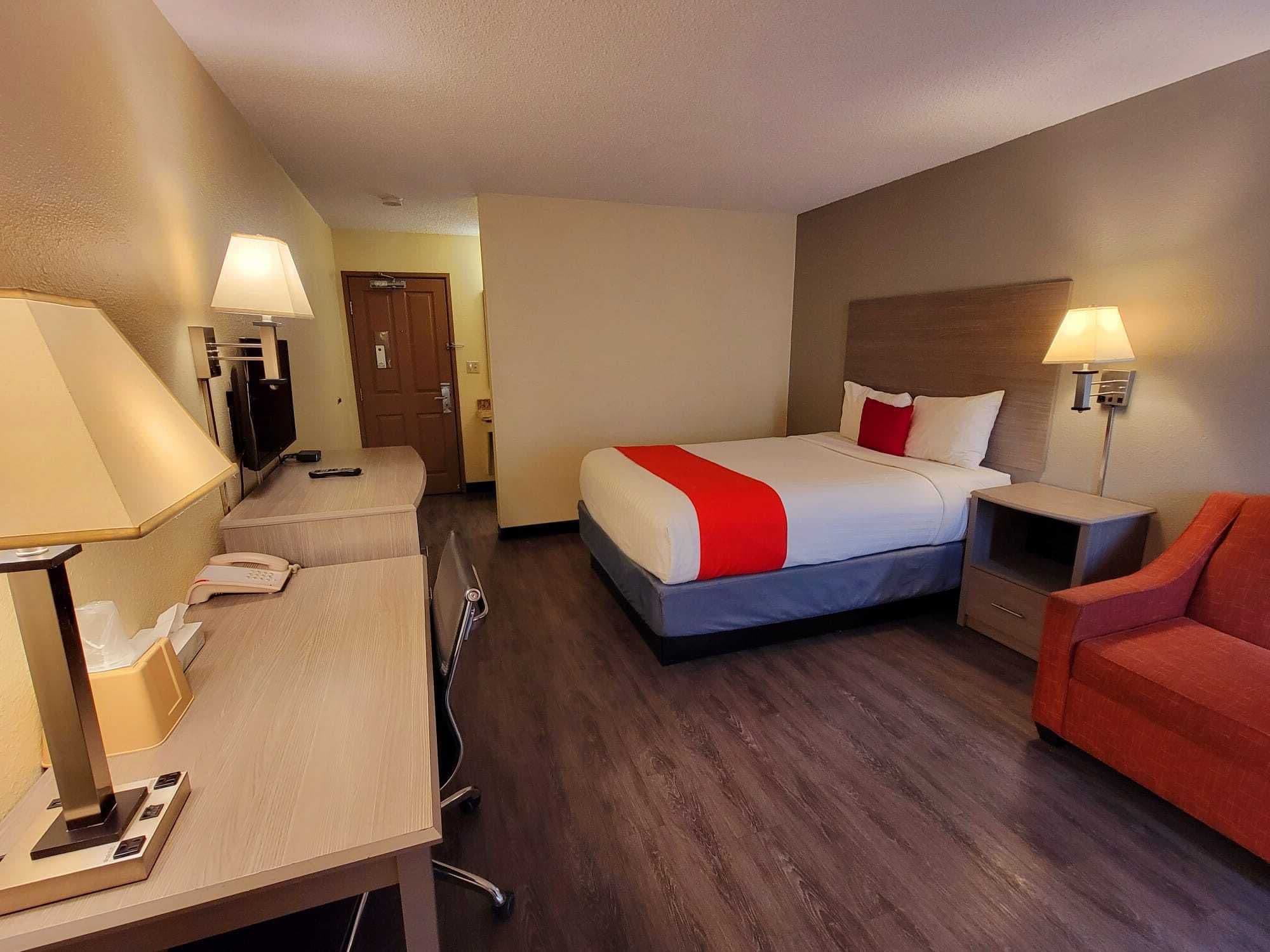 A hotel room with a bed, desk, chair, and a TV.