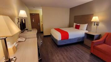A hotel room with a bed, desk, chair, and a TV.