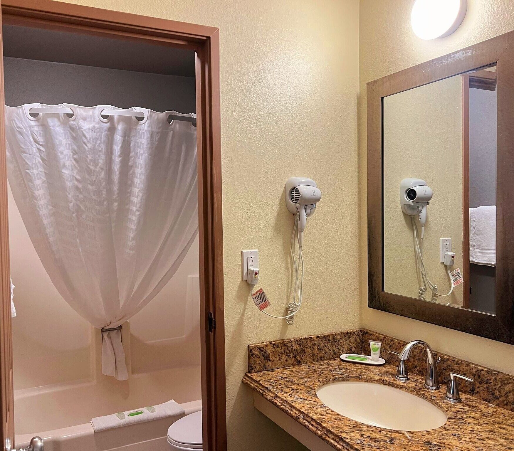 A bathroom with a shower curtain, a hairdryer, a sink, and a mirror.