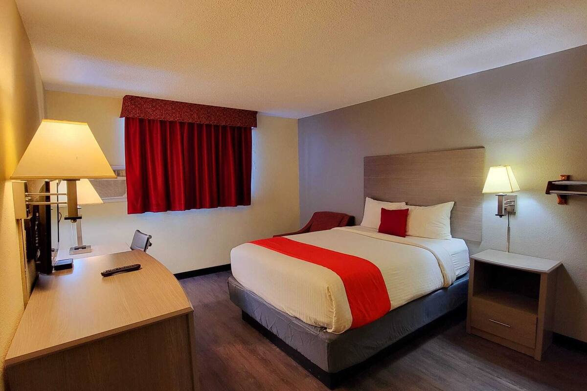 Een hotelkamer met een bed, nachtkastjes, een bureau en een raam met rode gordijnen.