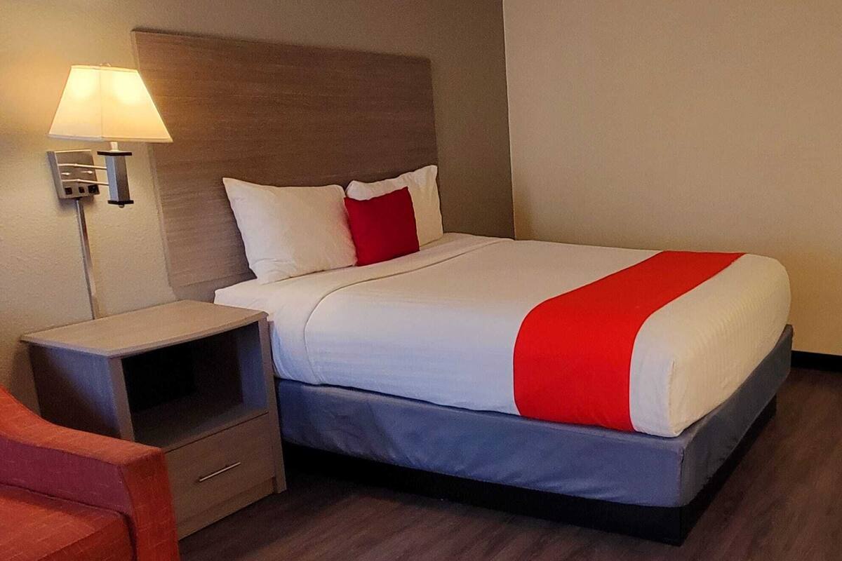 Een hotelkamer met een bed, nachtkastje, lamp en stoel.