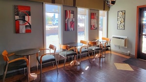 A modern interior with a seating area featuring round tables and chairs, large windows, and artwork on the walls.