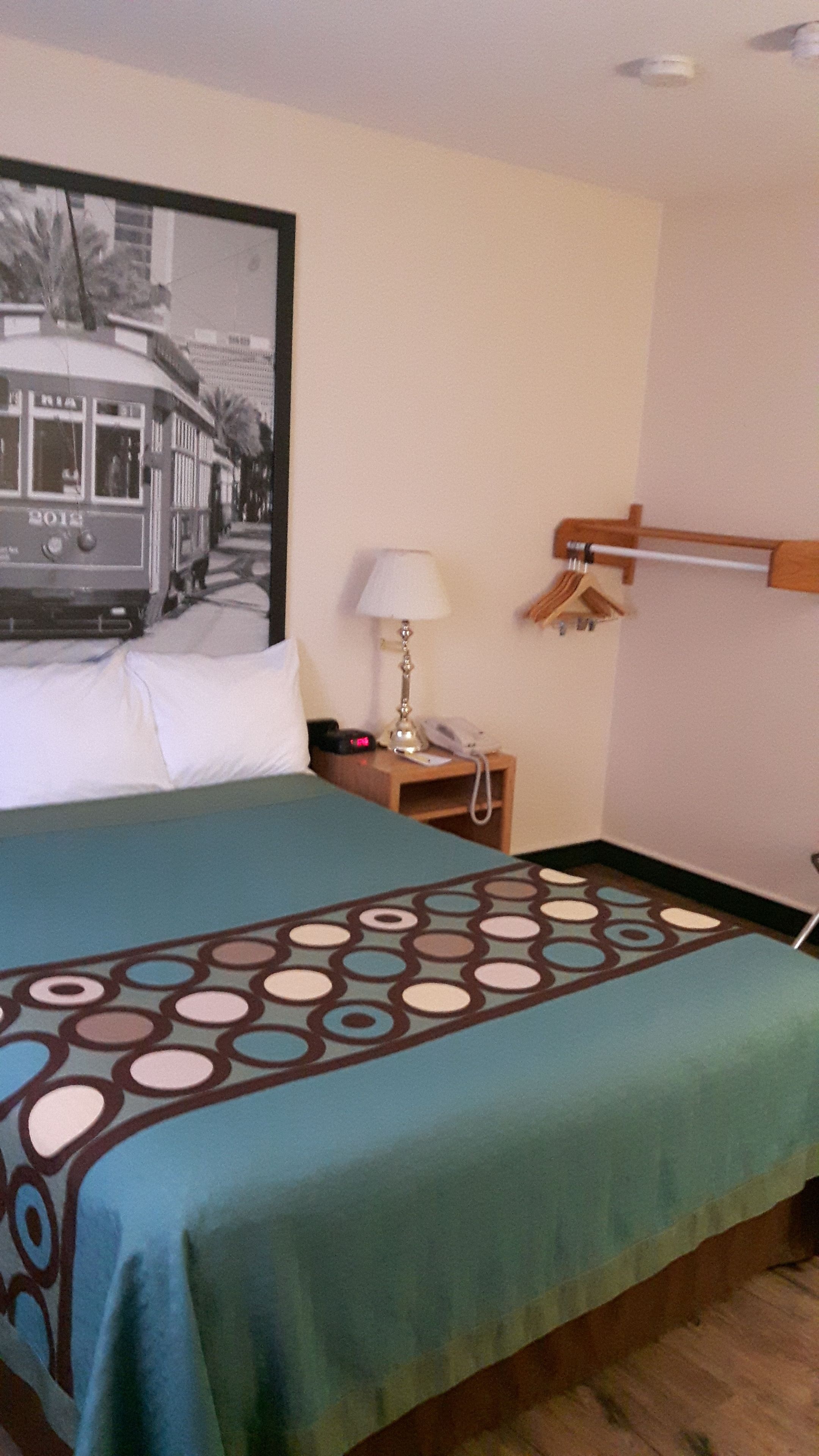 Una habitación de hotel con una cama, una mesita de noche, una lámpara, un teléfono y un gancho en la pared.