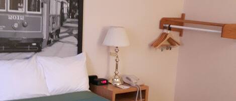 Una habitación de hotel con una cama, una mesita de noche, una lámpara, un teléfono y un gancho en la pared.