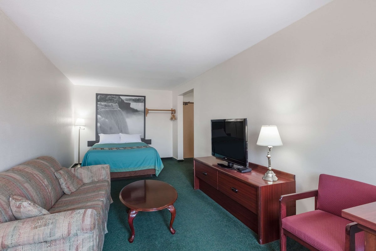 Una habitación de hotel con cama, televisor, escritorio con lámpara, sofá y una mesita.