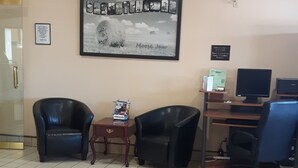 A reception area with two black leather chairs, a small wooden table with a snack package, a computer desk with a monitor, and a framed welcome sign on the wall. - Super 8 by Wyndham Moose Jaw SK (Moose Jaw)