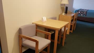 Une chambre d’hôtel avec une table et des chaises en bois, une lampe, un lit recouvert d’une couvre-lit à motifs et un tapis vert.