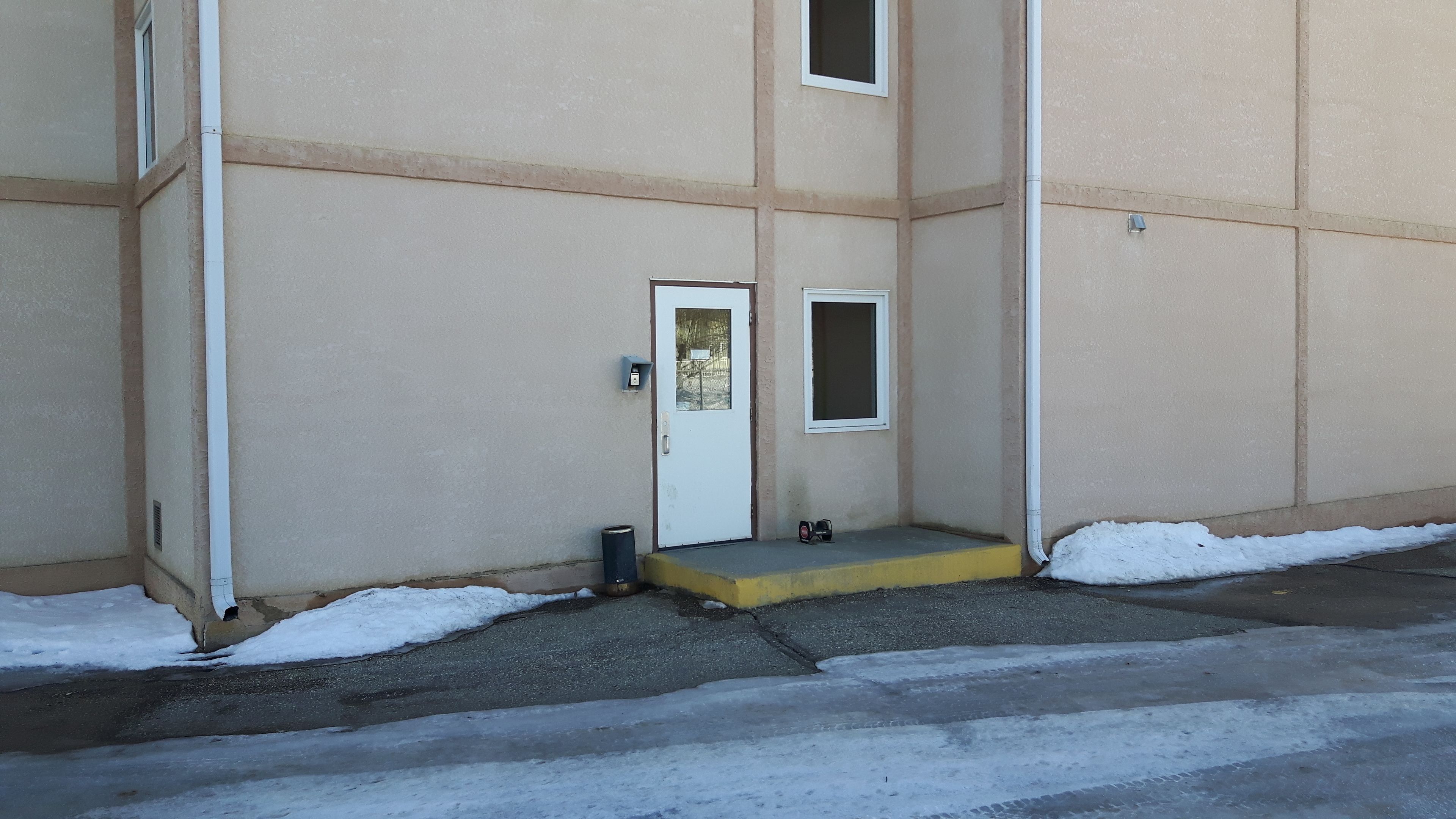 A building entrance with a white door, a small window, and a yellow step leading up to the door.