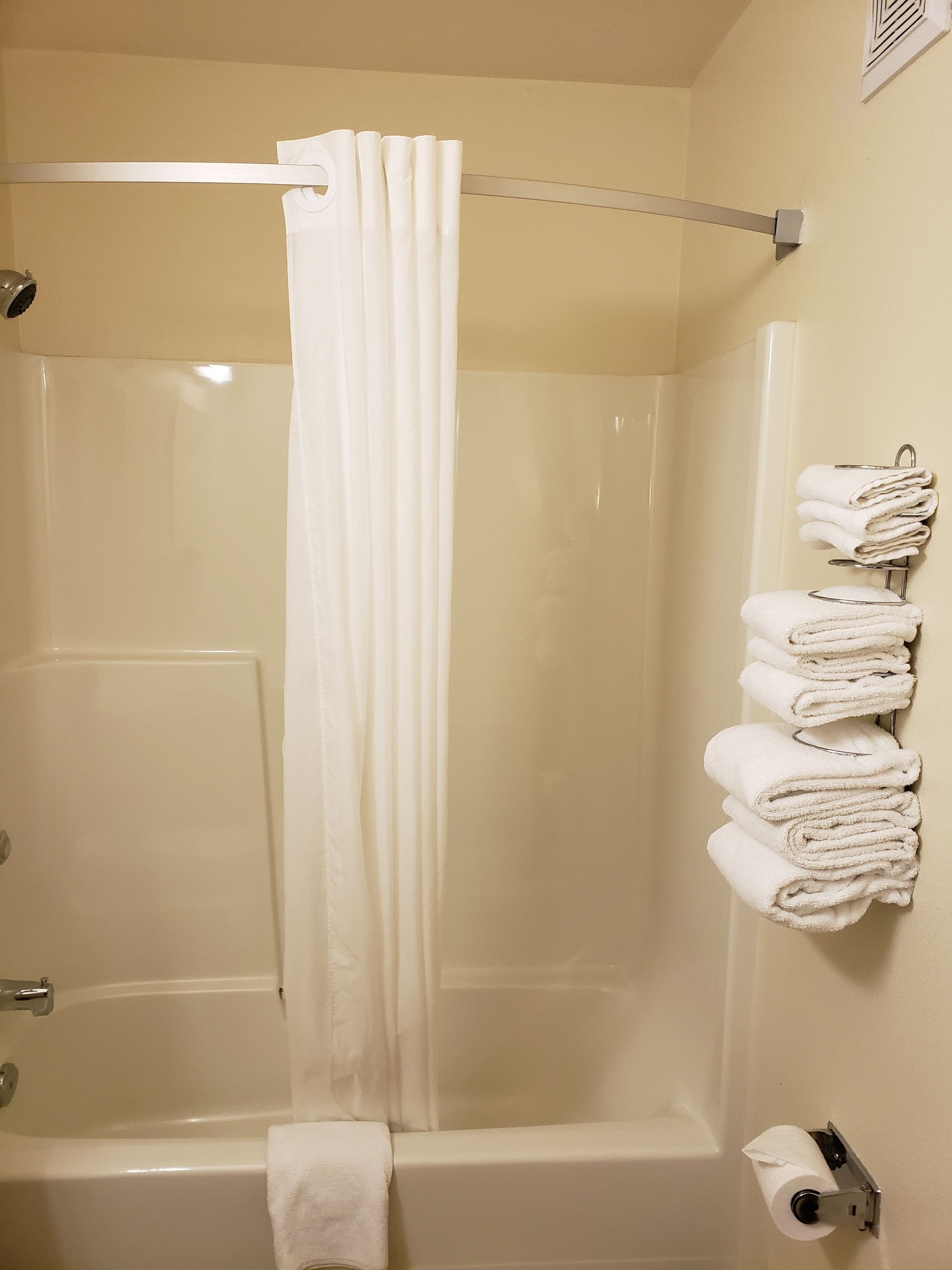 A bathroom with a glass shower enclosure, a towel rack with folded towels, and a toilet paper holder.