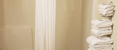 A bathroom with a glass shower enclosure, a towel rack with folded towels, and a toilet paper holder.