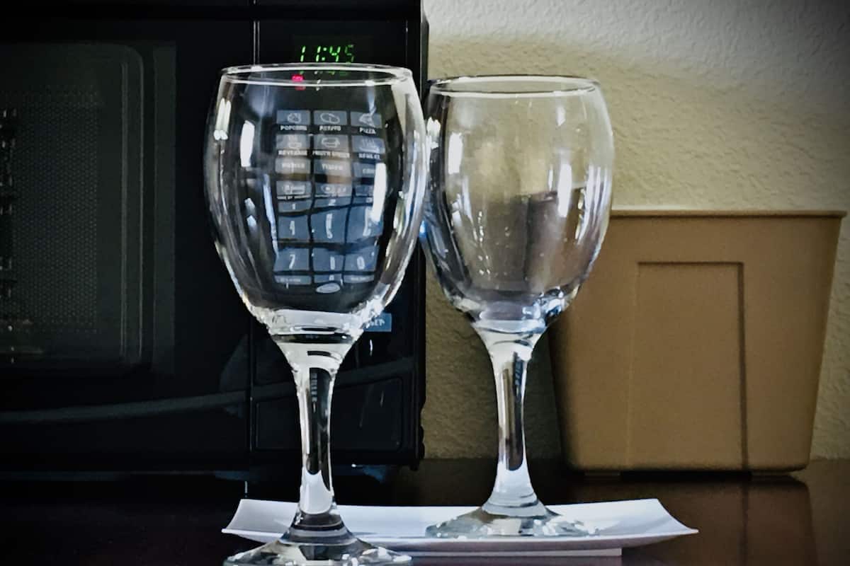 Dos copas de vino sobre una mesa, con un microondas al fondo.