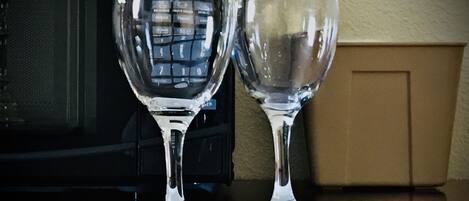 Two wine glasses on a table with a microwave in the background.