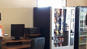 A room with a desk, computer, chair, and vending machines. - Super 8 by Wyndham Moose Jaw SK (Moose Jaw)