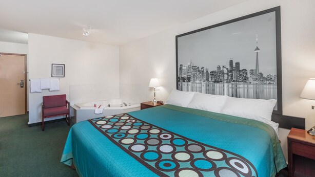A hotel room with a bed, a cityscape painting, a red chair, a desk, and a bathtub. - Super 8 by Wyndham Moose Jaw SK (Moose Jaw)