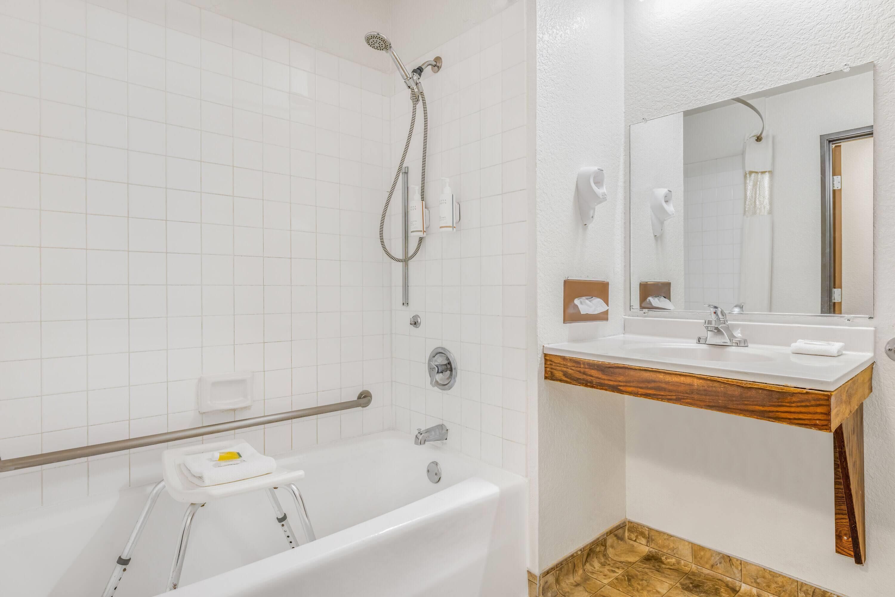 A modern bathroom with a white bathtub, a wooden vanity, a large mirror, and a shower with a handheld showerhead.