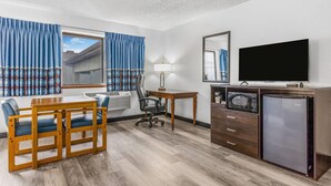 Habitación de hotel con una mesa de comedor de madera, dos sillas, un escritorio con lámpara, televisor de pantalla plana, refrigerador y microondas.